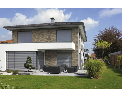 Maison individuelle moderne avec façade en brique et terrasse, équipée de volets roulants et de stores extérieurs gris.