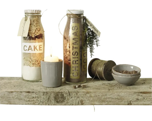 Deux bouteilles en verre avec préparations pour gâteaux, une bougie dans un pot, une bobine de fil et deux petits bols sur une planche en bois.