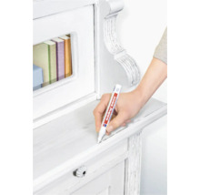 Une main utilise un marqueur pour meubles Edding 8900 pour retoucher une surface en bois blanc sur un meuble.