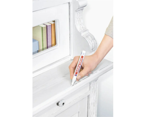 Une main utilise un marqueur pour meubles Edding 8900 pour retoucher une surface en bois blanc sur un meuble.