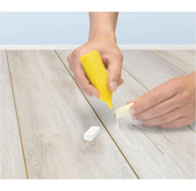Eine Person repariert einen Laminatboden mit einem Reparaturwachs und einem Schmelzer.