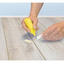 Person verwendet ein Reparaturset mit Wachsstift zum Ausbessern von Kratzern und Beschädigungen auf einem Laminatboden oder Parkettboden.