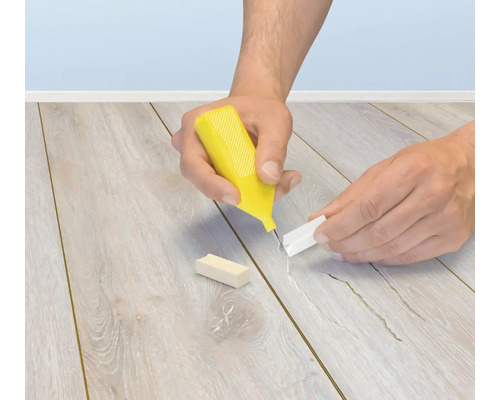 Person verwendet ein Reparaturset mit Wachsstift zum Ausbessern von Kratzern und Beschädigungen auf einem Laminatboden oder Parkettboden.