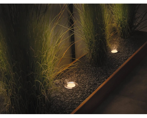 Spots encastrés modernes dans une jardinière remplie de gravier éclairant des herbes ornementales pendant la nuit.