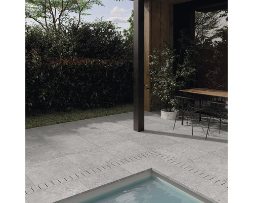 Terrasse mit grauen Steinoptik Fliesen um einen Pool, angrenzend an ein modernes Haus mit Sitzbereich im Außenbereich.