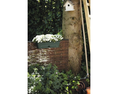 Gartenszene mit Flechtzaun, bepflanztem Blumenkasten, Baumstamm und Vogelhaus