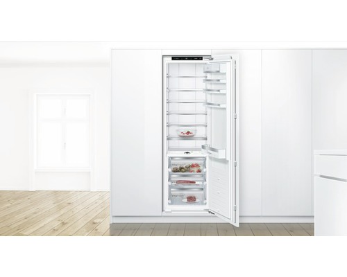 Réfrigérateur encastrable avec porte ouverte et plusieurs étagères pour le stockage des aliments dans une cuisine lumineuse.