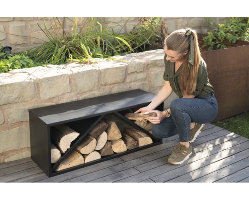 Frau legt Holz in ein schwarzes Holzregal im Garten