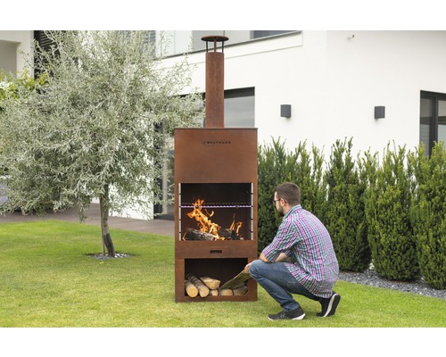 Mann legt Holz in einen Westmann Grillkamin im Garten.