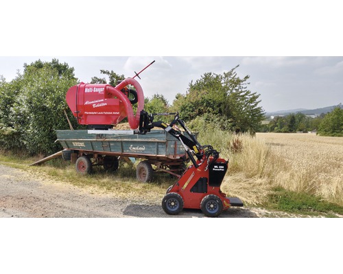 Roter Mini-Lader mit montiertem Laubsauger befüllt Anhänger mit Pferdeäpfeln, Laub und Fallobst