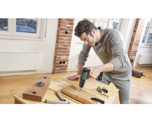 Un homme perce un trou dans une planche de bois avec une perceuse.