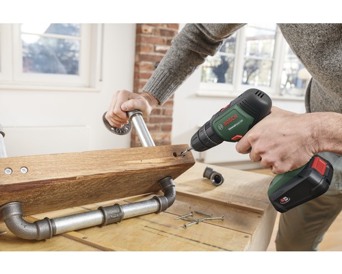 Une personne perce un trou dans une planche en bois avec des raccords de tuyaux à l'aide d'une perceuse sans fil.