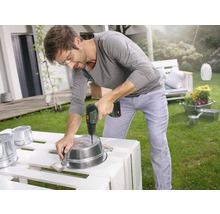 Un homme perce des trous dans un seau en métal dans le jardin avec une perceuse-visseuse sans fil.