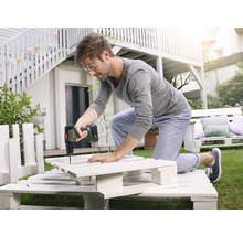 Un homme travaille avec une visseuse sans fil sur un projet de bricolage à partir de palettes dans le jardin.