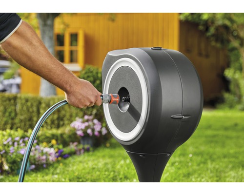 Gartenszene mit Schlauchbox und Person, die einen Gartenschlauch anschliesst.