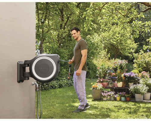 Mann benutzt eine an der Wand montierte Gardena Schlauchtrommel im Garten