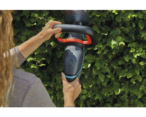 Une personne utilise un taille-haie sans fil Gardena devant une haie.