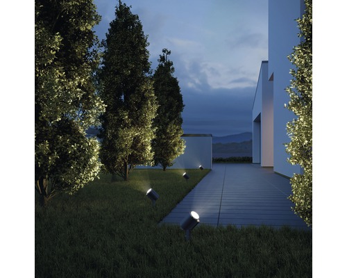 Extérieur d''une maison moderne avec pelouse et arbres éclairés par plusieurs projecteurs.