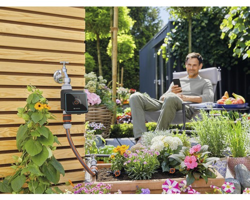 Gartenbewässerungssystem mit digitaler Steuerung und entspanntem Mann im Hintergrund