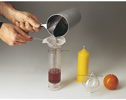 Personne versant de la cire à travers un tamis dans un moule à bougie, à côté de bougies finies