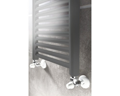 Radiateur sèche-serviettes gris avec robinets de radiateur sur un mur carrelé