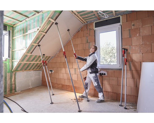 Un artisan monte une plaque de plâtre avec des supports télescopiques dans un aménagement de combles.