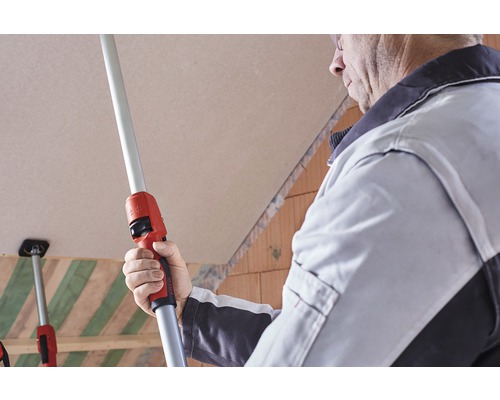 Un artisan utilise une perche télescopique pour fixer des plaques de plâtre à un plafond.