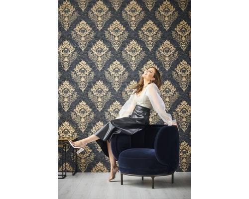 Frau sitzt auf einem Sessel vor einer Wand mit gemusterten Tapeten