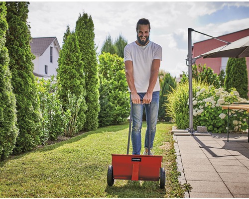 Un homme utilise un épandeur d''engrais dans le jardin.
