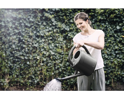 Frau giesst mit einer Giesskanne Pflanzen im Garten