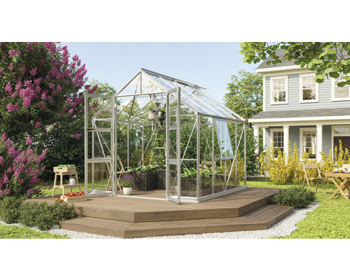 Gewächshaus Vitavia Olymp 6700 Einscheibensicherheitsglas 3 mm 257 x 258 cm silber Gewächshaus auf Holzterrasse in einem Garten mit Pflanzen und einem Haus im Hintergrund.