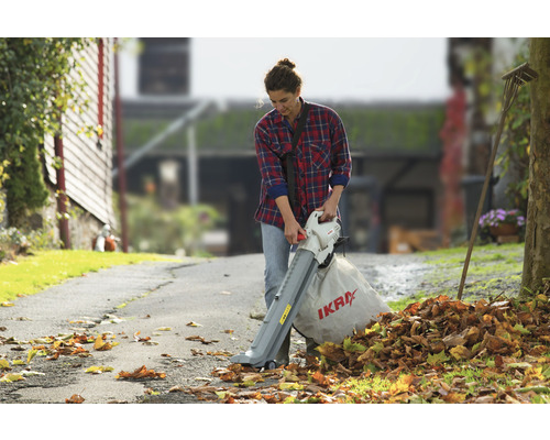 Une femme utilise un aspirateur de feuilles dans le jardin pour enlever les feuilles mortes.