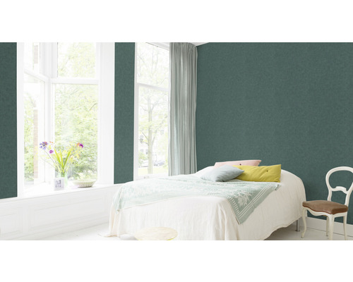 Schlafzimmer mit grüner Vliestapete, Bett, Fenster und Stuhl.