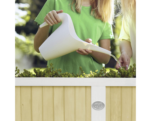 Kind giesst Pflanzen mit einer Gießkanne in einem Hochbeet.