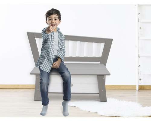 Garçon assis sur un banc coffre à jouets gris dans une chambre d''enfant