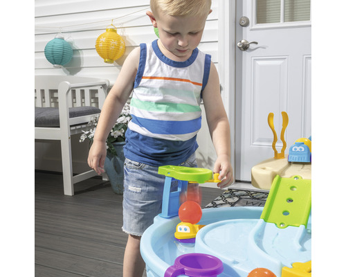 Enfant jouant avec une table de jeu d''eau extérieure sur une terrasse.