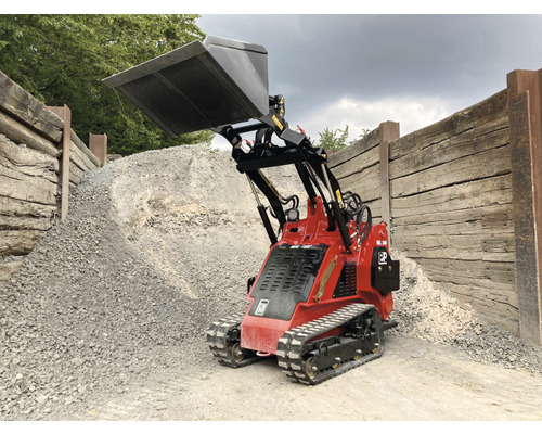 Mini-chargeuse rouge avec godet devant un tas de gravier