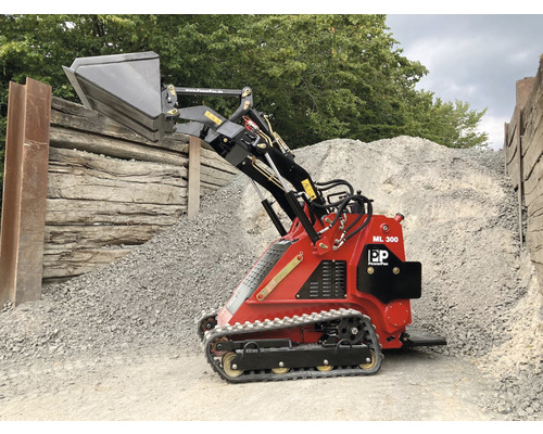 Mini-chargeuse compacte rouge avec godet devant un tas de gravier.