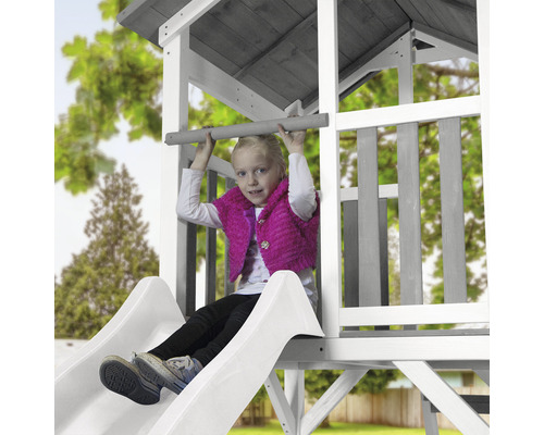 Mädchen auf einer Rutsche in einem Spielhaus aus Holz.
