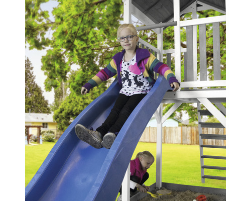 Mädchen rutscht auf einer blauen Rutsche eines Spielturms im Garten.