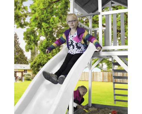 Une fille glisse sur un toboggan blanc d''une tour de jeux dans le jardin.