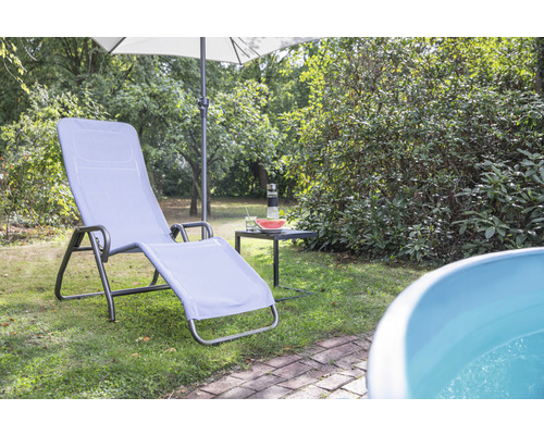 Scène de jardin avec chaise longue, parasol et petite table sur une pelouse