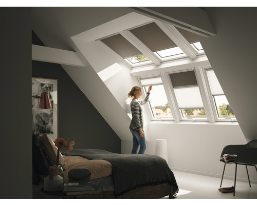 Frau bedient Dachfensterrollos im Schlafzimmer
