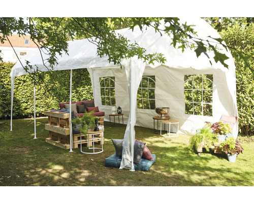 Scène avec tente de réception blanche, mobilier de palettes et décoration de jardin sur une pelouse