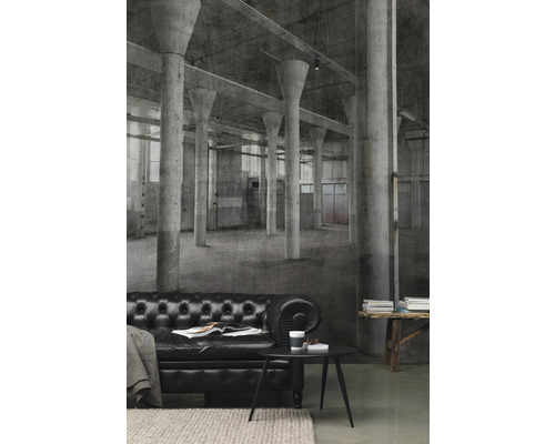 Salon avec canapé en cuir noir devant un papier peint photo avec un motif de halle d''usine