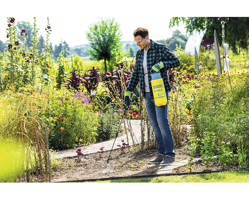 Ein Mann verwendet eine Gloria Gartenspritze in einem blühenden Garten.