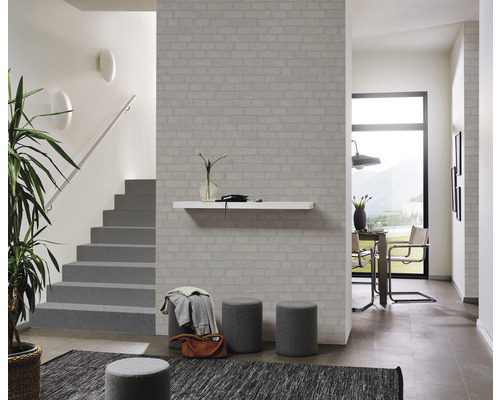 Couloir lumineux avec papier peint imitation briques, escalier, table et chaises.