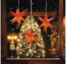 Drei rote Sterne als Fensterdekoration vor verschneiter Landschaft und Weihnachtsbaum