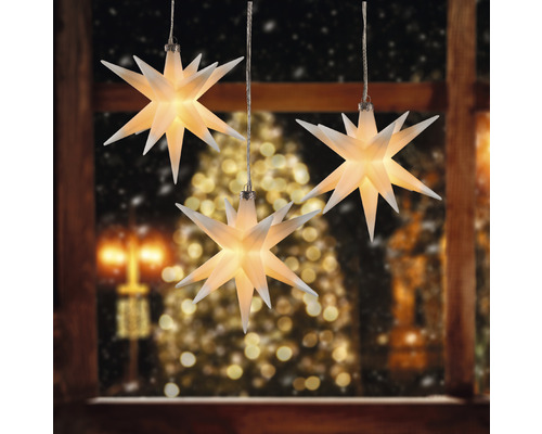 Drei leuchtende Sterne als Dekoration vor einem Fenster zur Weihnachtszeit.