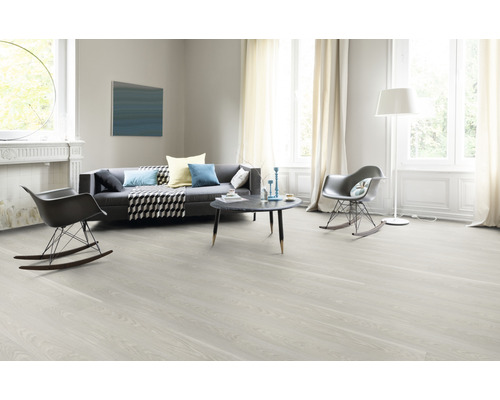 Salon lumineux avec plancher, canapé et fauteuils.